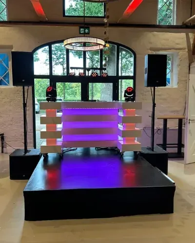 DJ set huren: verlichte DJ-booth op een podium in een feestzaal