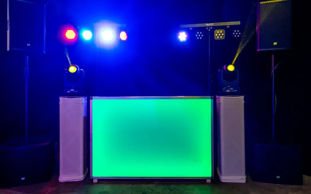 Muziekinstallatie huren: groen verlichte DJ-booth met speakers en lichteffecten